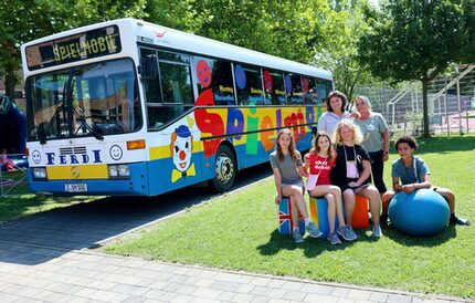 Juliane Nestler (Amt für Umwelt und Stadtplanung / Grafikerin) und Angela Herz (Amt für Familie, Schule und Soziales / pädagogische Leiterin Spielmobil) posieren mit Spielstadt-Kindern vorm neu gestalteten Bus